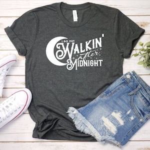 May include: A dark gray t-shirt with a white graphic that says "I go out walkin' after midnight" with a crescent moon and stars.