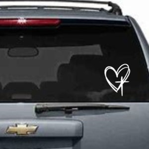 May include: White vinyl decal of a heart with a cross inside. The decal is on the back window of a gray SUV.