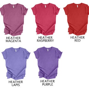 May include: Five heathered t-shirts in various colors: heather magenta, heather raspberry, heather red, heather lapis, and heather purple. Each shirt is a solid color with a crew neck.