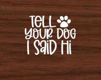 May include: A dark brown background with white text saying "Tell your dog I said Hi", accompanied by a paw print. The text is in a friendly, handwritten font, suitable for pet owners.