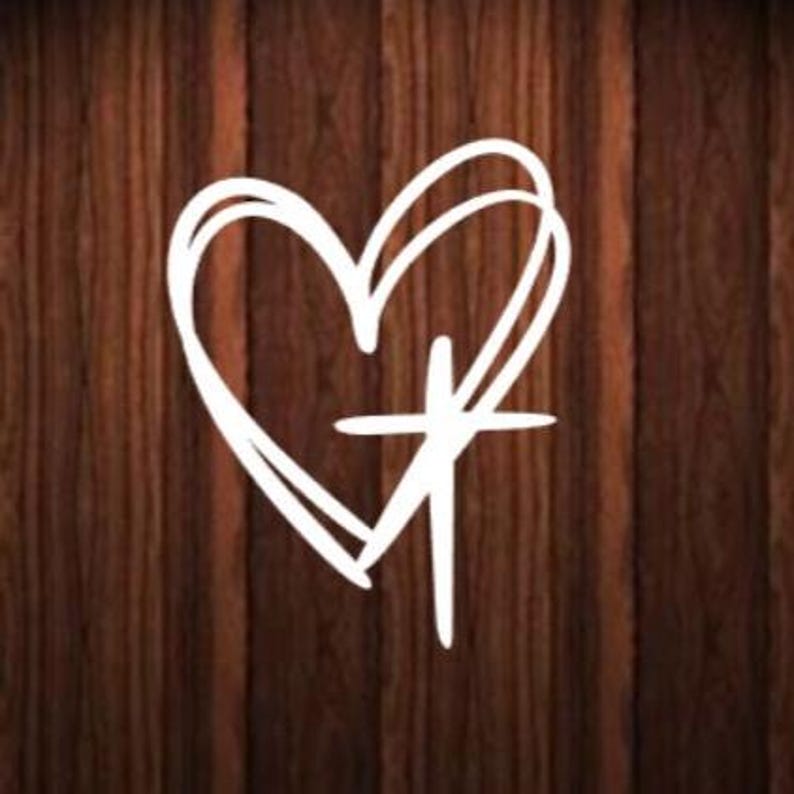 May include: A white heart with a cross inside, on a brown wood background.