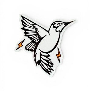 May include: A white hummingbird sticker with black outline and details, wings spread in flight. Two orange lightning bolts flank the bird. The sticker is on a white background.