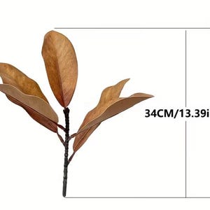 May include: A brown artificial magnolia leaf stem featuring four broad, dried-look leaves attached to a central dark brown branch. The stem measures 13.39 inches in total height as indicated by the measurement lines and text on the right side.