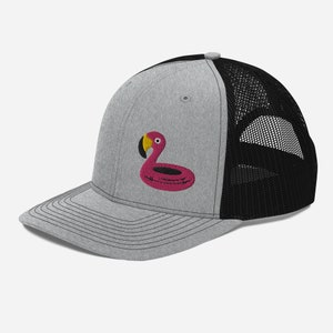 Könnte beinhalten: Eine graue und schwarze Trucker-Kappe mit einem gestickten pinkfarbenen Flamingo-Schwimmring auf der Vorderseite.
