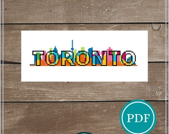 May include: A cross-stitch pattern for instant download featuring the Toronto skyline. The word "TORONTO" is displayed in colorful pixelated letters. The pattern size is 4" x 10" and is recommended for 14 ct. A PDF icon is visible.