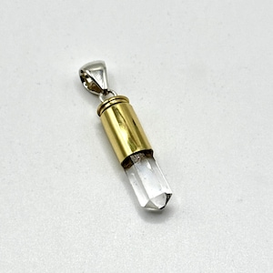 May include: A pendant featuring a clear quartz crystal encased in a gold-colored metal cylinder. The pendant has a silver-colored bail for attaching to a chain. The crystal is faceted at the bottom.
