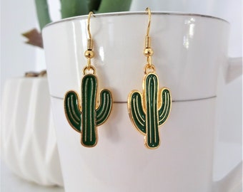 May include: A pair of gold cactus earrings with green enamel. The earrings are dangle style with a hook closure.