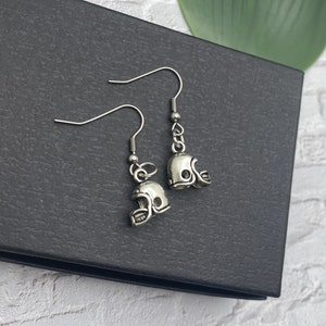 May include: A pair of silver earrings with football helmet charms. The earrings are on a black background.