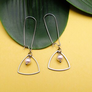 May include: A pair of silver earrings with a triangle shape and a single white pearl hanging from each.