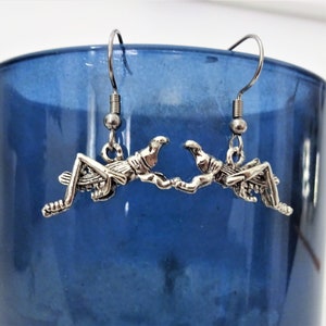 May include: A pair of silver earrings featuring a detailed grasshopper design. The earrings are hanging from silver hooks.