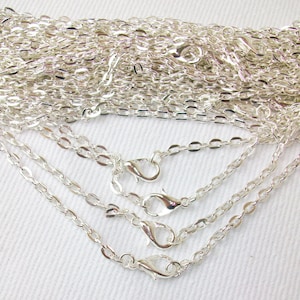 May include: A close-up of a pile of silver chain necklaces with lobster claw clasps. The chains are arranged in a fan shape, with the ends of the chains overlapping.