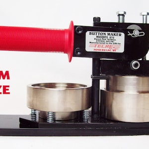 Op de afbeelding: Een zwarte knopenmaker met een rode handgreep. De machine is gelabeld "BUTTON MAKER MODEL 275" en "Manufactured in the USA by TELPAC FOND DU LAC WI".