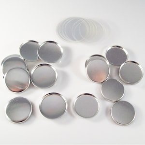 May include: A set of 10 silver-colored round metal containers with lids. The containers are arranged in a semi-circle on a white surface. There are also 10 clear plastic round lids in the background.