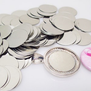 May include: A pile of silver metal circles, a silver metal pendant with a blank circle, and a pink button with a pink ribbon.