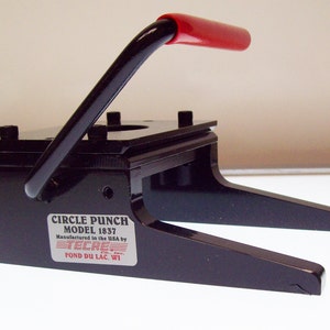 May include: Black metal circle punch with a red handle. The punch is labeled "CIRCLE PUNCH MODEL 1837 Manufactured in the USA by TECR, INC. FOND DU LAC, WI."