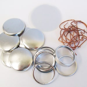 May include: A set of silver button making supplies, including 1 inch round metal button bases, metal button backs, and copper wire loops.