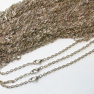 May include: A silver chain with a lobster clasp. The chain is coiled up and there are three separate chains laid out straight.