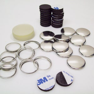 May include: Assortment of silver metal button parts for crafting, including a stack of round black adhesive-backed discs, a stack of white plastic discs, and a stack of adhesive-backed 3M double-sided tape.