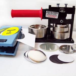 May include: A black button maker with a red handle, a blue button press, and various button parts including white, black, and silver circles. The button maker has a label that reads "Button Maker Model BB51 Photo Patent No. 6039944 Manufactured in the USA TECHRE FIND ON LAF. W1".