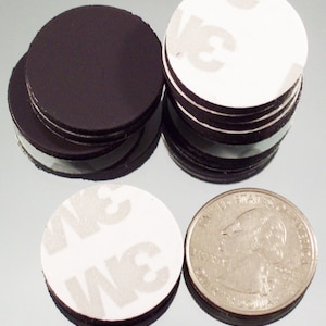 May include: A stack of round black adhesive-backed magnets with a white adhesive backing. The magnets are about the size of a US quarter.