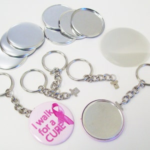 May include: A set of silver metal button blanks, a clear plastic button blank, and two keychains with a pink button that says "I walk for a CURE" and a pink ribbon.