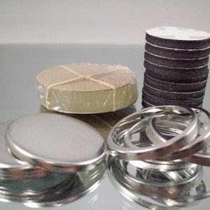 May include: A set of silver-colored metal lids, a stack of round black and white adhesive-backed discs, and a stack of round beige discs wrapped in clear plastic.