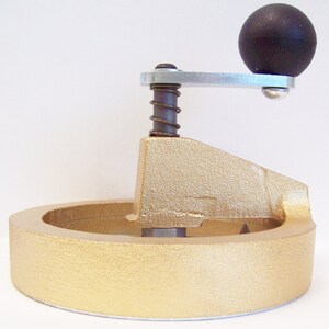 May include: A gold-colored metal circle cutter with a black handle and a spring-loaded mechanism. The cutter is used to create circles in materials like paper, fabric, and leather.