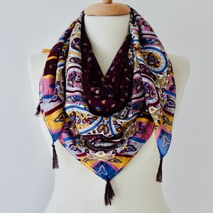 May include: A colorful paisley patterned scarf with tassels on the ends. The scarf is displayed on a white mannequin.
