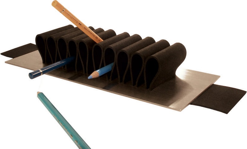 Puede incluir: Un porta l&aacute;pices de espuma negra con una base de metal y una tira de espuma negra en el lateral. El porta l&aacute;pices tiene m&uacute;ltiples ranuras para l&aacute;pices y est&aacute; dise&ntilde;ado para mantener los l&aacute;pices en posici&oacute;n vertical. Hay tres l&aacute;pices en el porta l&aacute;pices, uno marr&oacute;n y dos azules.