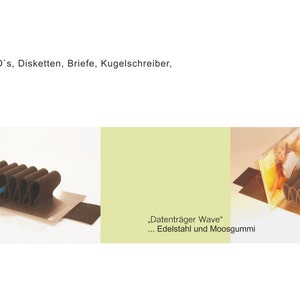 Puede incluir: Un organizador de escritorio de color marr&oacute;n, en forma de onda y con m&uacute;ltiples secciones, hecho de acero inoxidable y gomaespuma. El organizador est&aacute; dise&ntilde;ado para contener CD, disquetes, cartas, bol&iacute;grafos y llaves. El texto "Datentr&auml;ger Wave" est&aacute; impreso en el organizador, junto con las palabras "Edelstahl und Moosgummi".