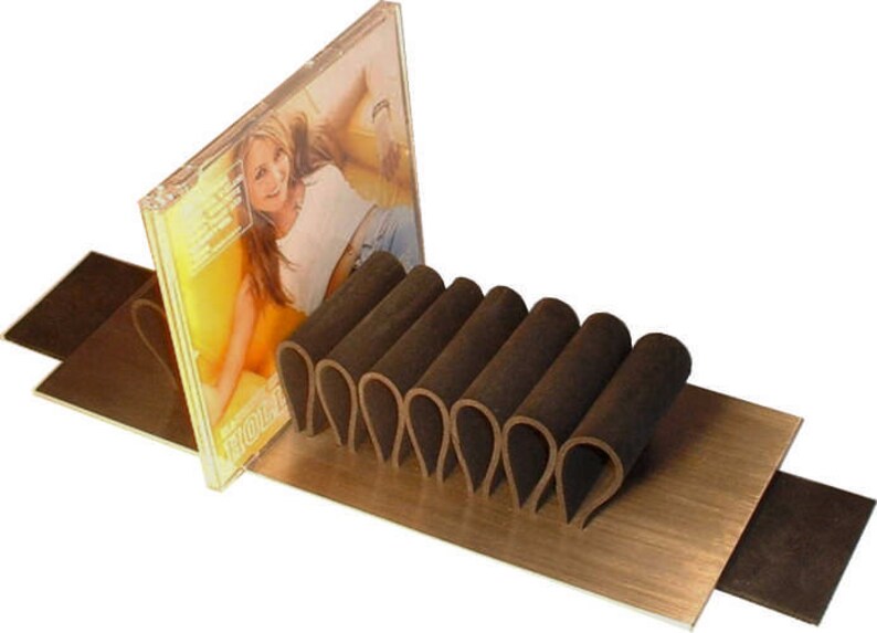 Puede incluir: Un soporte de CD de cuero marr&oacute;n con una caja de CD que presenta a una mujer en la portada. El soporte de CD est&aacute; hecho de m&uacute;ltiples bucles de cuero y est&aacute; sentado sobre una superficie de madera.