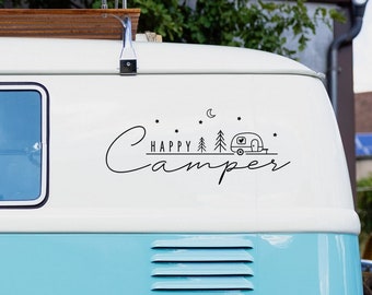 Op de afbeelding: Een lichtblauwe vintage bestelwagen met een wit dak en een zwarte sticker met de tekst "Happy Camper" met een kleine camper en dennenbomen. De bestelwagen heeft een witte band met een chromen wieldoppen.