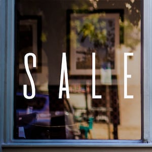 May include: A shop window with the word "SALE" displayed in large white letters. The window is blurred, showing a glimpse of the shop's interior.
