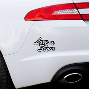 May include: A white car with a black vinyl decal that says "Low n Slow" on the rear bumper.