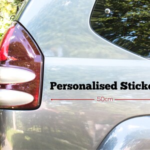 May include: A grey car with a black "Personalised Sticker" decal on the back. The sticker is 50 cm wide.
