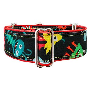 May include: A black pet collar featuring a colorful pattern of cartoon monsters in shades of blue, green, yellow, and red. The collar is edged with red fabric, accented by yellow stitching, and includes a silver metal adjustable slider buckle.