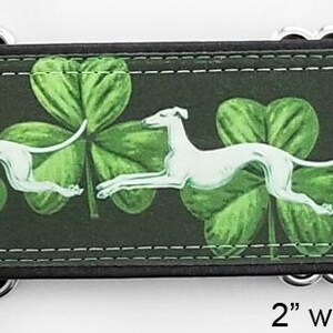 May include: A 2-inch wide dog collar featuring a repeating pattern of white greyhound silhouettes running across a dark background with green shamrocks. The collar includes silver-toned metal hardware and a black satin lining for comfort.