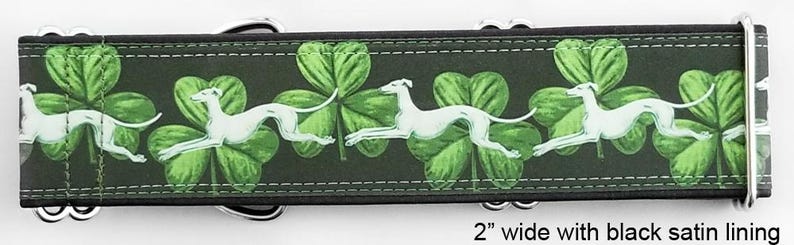 May include: A 2-inch wide dog collar featuring a repeating pattern of white greyhound silhouettes running across a dark background with green shamrocks. The collar includes silver-toned metal hardware and a black satin lining for comfort.