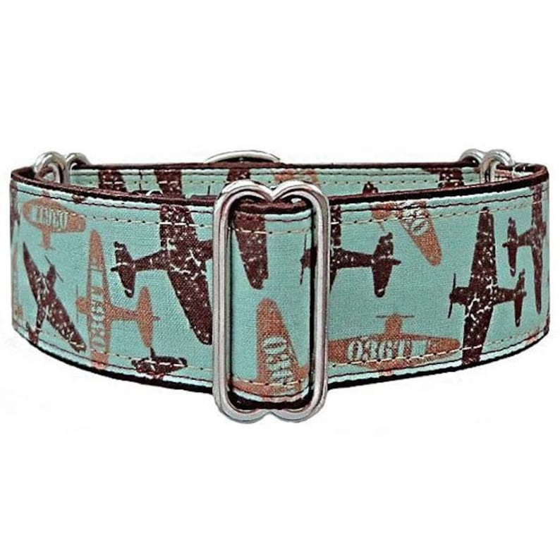 May include: A dog collar with a light teal background and a repeating pattern of brown and tan airplanes. The collar has a silver metal buckle and hardware. The collar is approximately 1 inch wide.