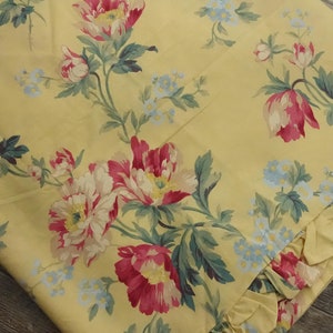 May include: Yellow fabric with a floral pattern featuring pink and white flowers with green leaves. The fabric has a ruffled edge.