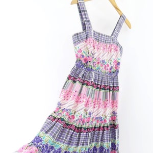Op de afbeelding: Een gelaagde maxi-jurk met een bloemenprint in roze, paarse en groene tinten. De jurk heeft een vierkante halslijn en dunne bandjes.