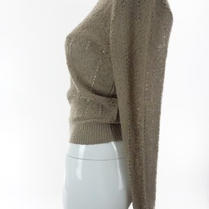 May include: A beige knitted sweater with a delicate openwork pattern. The sweater has long sleeves and a round neckline.
