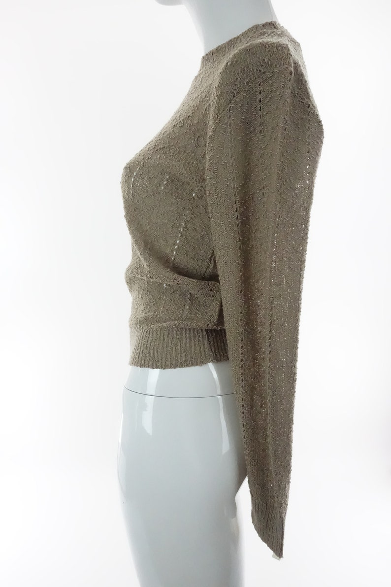 May include: A beige knitted sweater with a delicate openwork pattern. The sweater has long sleeves and a round neckline.