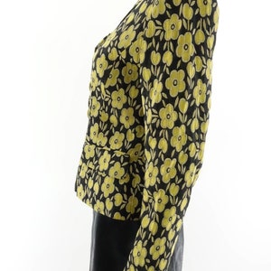 Puede incluir: Una chaqueta negra con estampado floral amarillo, manga larga y cierre de botones.