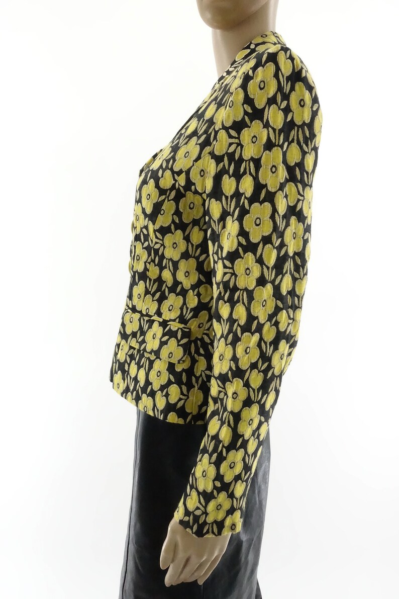 Puede incluir: Una chaqueta negra con estampado floral amarillo, manga larga y cierre de botones.