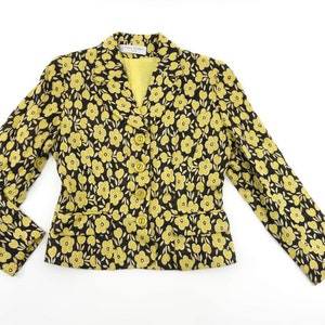 Puede incluir: Una chaqueta negra con estampado floral amarillo y cierre de botones.