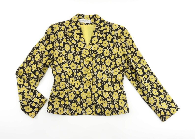 Puede incluir: Una chaqueta negra con estampado floral amarillo y cierre de botones.