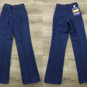 May include: A pair of dark blue denim jeans with a wide leg and a straight fit. The jeans have a button fly and belt loops. The jeans have a Wrangler label on the back pocket.