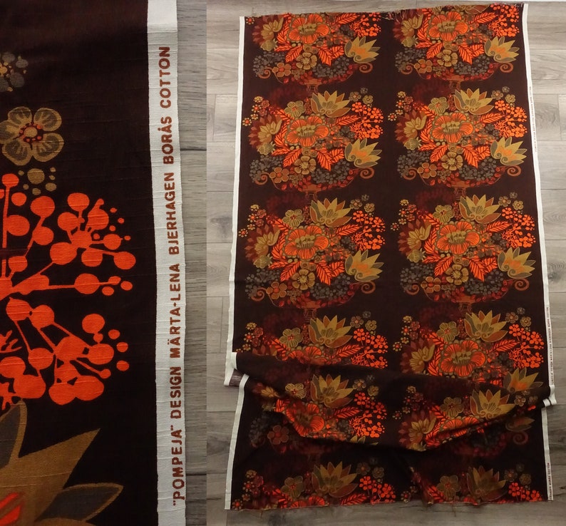 May include: A brown fabric with a repeating pattern of orange and brown flowers. The fabric has a white label with the text "POMPEJA DESIGN MARTA-LENA BJERHAGEN BOR&Aring;S COTTON".