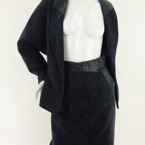 May include: A navy blue skirt suit with a black leather trim on the collar and pockets. The skirt has a black leather belt.